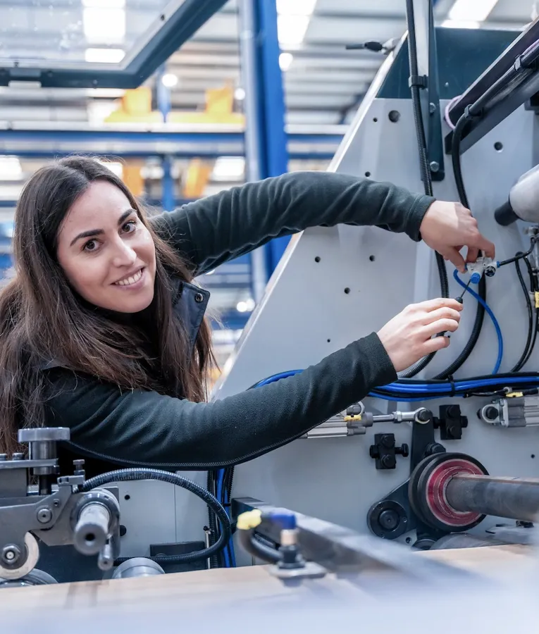 Kvinnlig tekniker arbetar med maskinutrustning i fabrik, schemalagd med workforce management och uppgiftsbaserad tidrapportering i tillverkning.