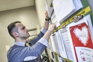 Butikschef går igenom schema och arbetsdokument på anslagstavlan för att säkerställa korrekt tidrapportering och bemanning.