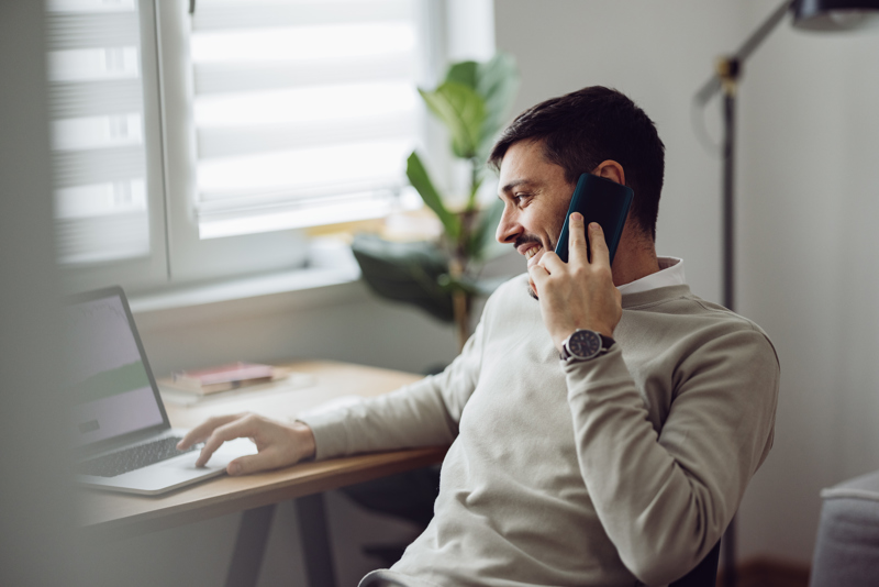 Man arbetar hemifrån med laptop och telefon medan han planerar arbetspass och hanterar tidrapportering via en AI-baserad workforce management-lösning.