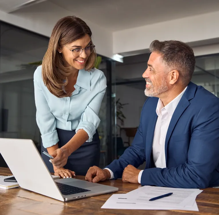 Leende affärsproffs samarbetar på ett modernt kontor och diskuterar data på en bärbar dator. Symboliserar teamwork, ledarskap och effektiv personalhantering.