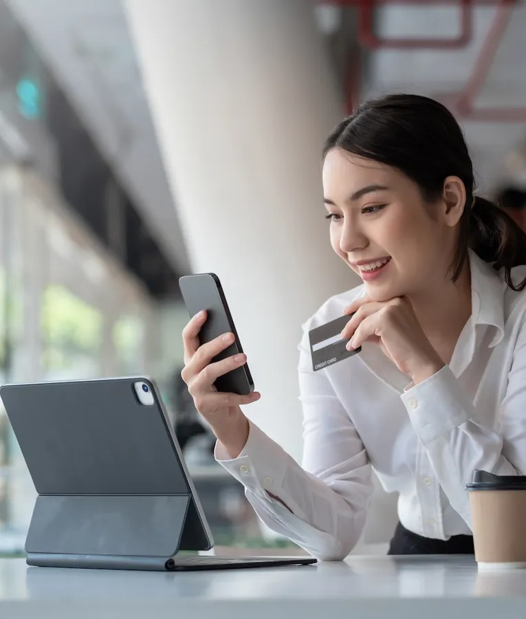 Leende affärskvinna använder en smartphone och kreditkort för en online-transaktion, med en surfplatta och kaffe på bordet, vilket representerar säker digital betalning.