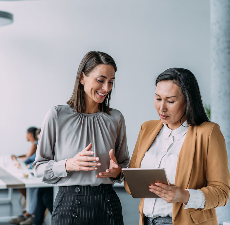 Två professionella kvinnor samarbetar med en surfplatta i en modern kontorsmiljö.