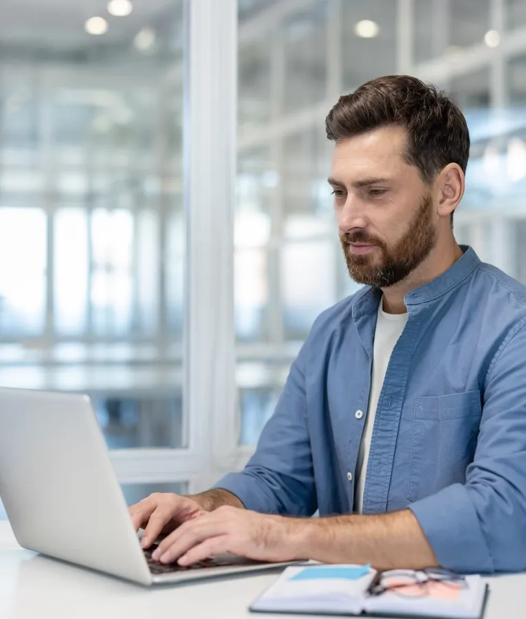 Kontorsanställd arbetar på laptop i en modern miljö med digital workforce management för schemaläggning, tidrapportering och HR-planering.