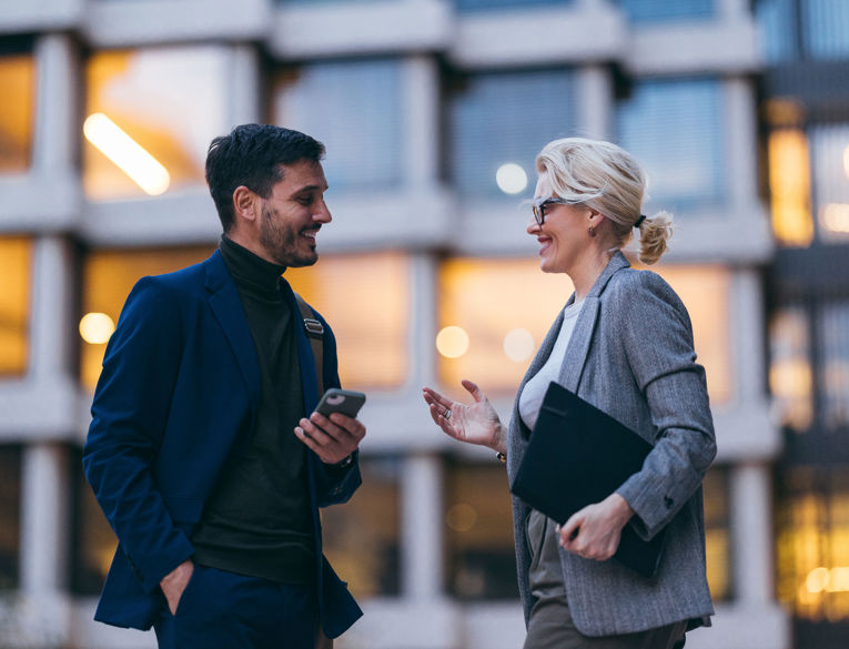 Två kollegor i en affärsmiljö som diskuterar arbetsstyrning, schemaläggning och tidsregistrering med hjälp av en mobil enhet