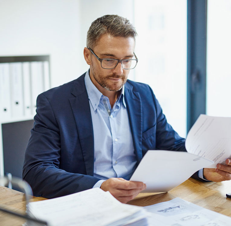 Man i kostym som granskar dokument vid ett skrivbord, vilket symboliserar professionalism och strategisk arbetsstyrning och schemaläggning